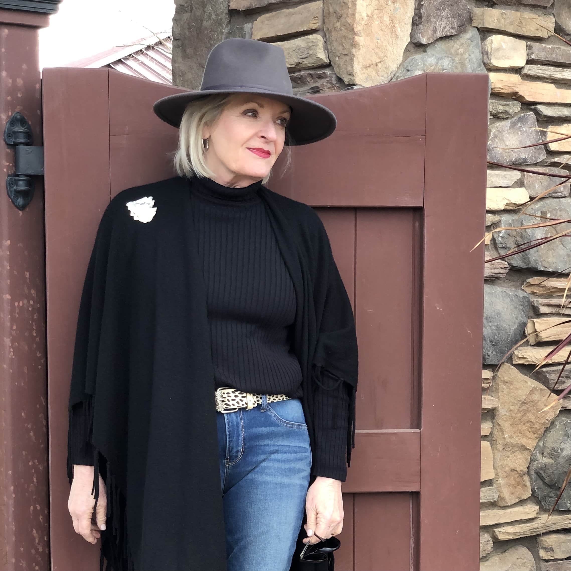 over 50 fashion blogger jennifer connolly wearing gray fedora, black ruana and blue jeans