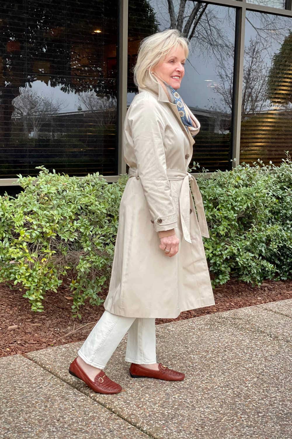 woman wearing pale khaki trench coat from Loft over pale beige jeans and bronw driving mocs