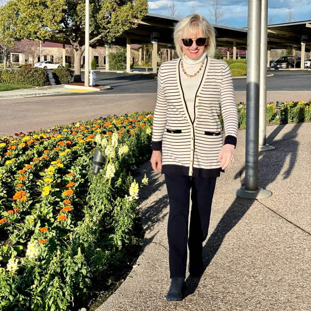 blonde woman wearing striped sweater and navy pants walking in the sun
