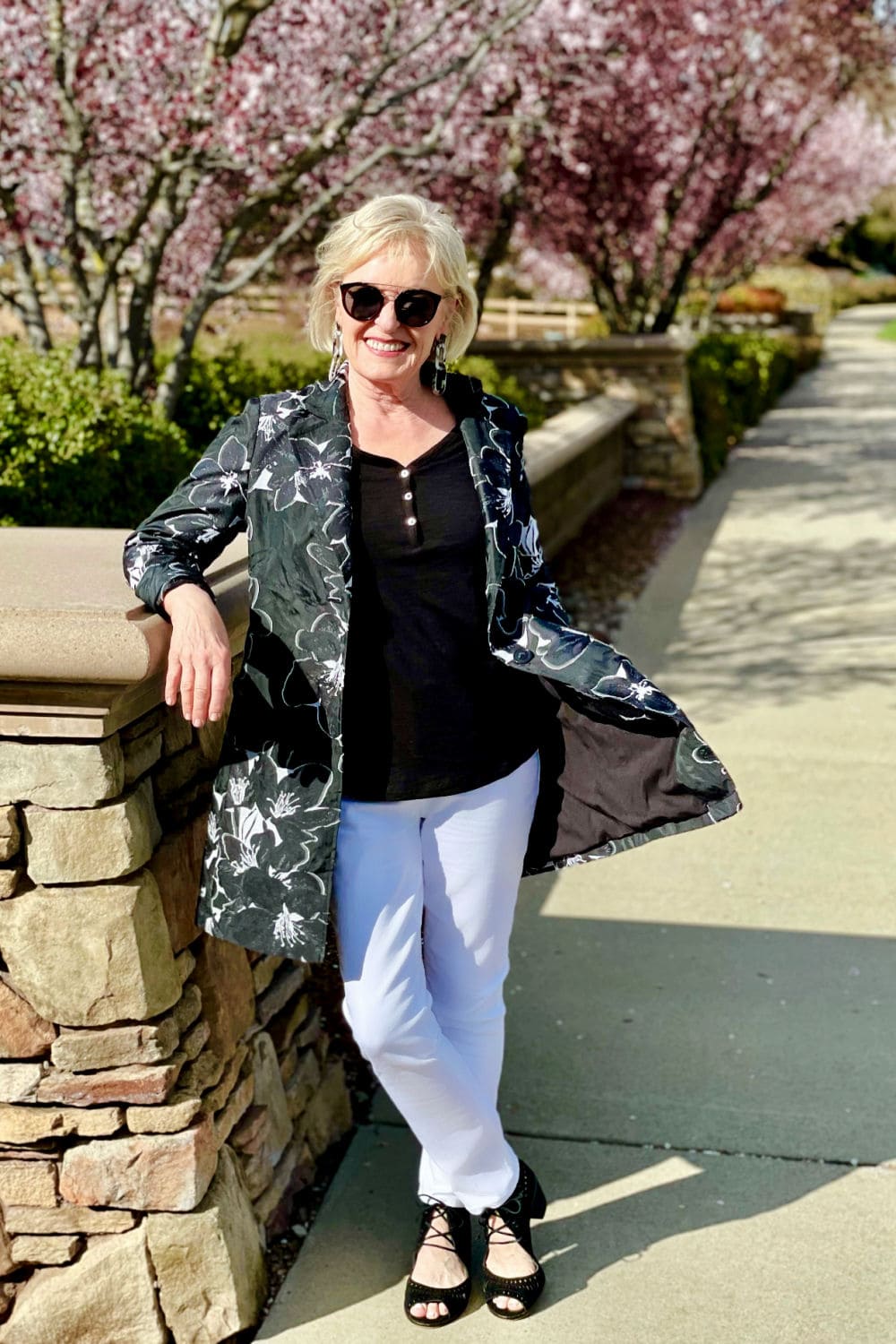 over 50 fashion blogger wearing black top, white jeans and leaning against wall
