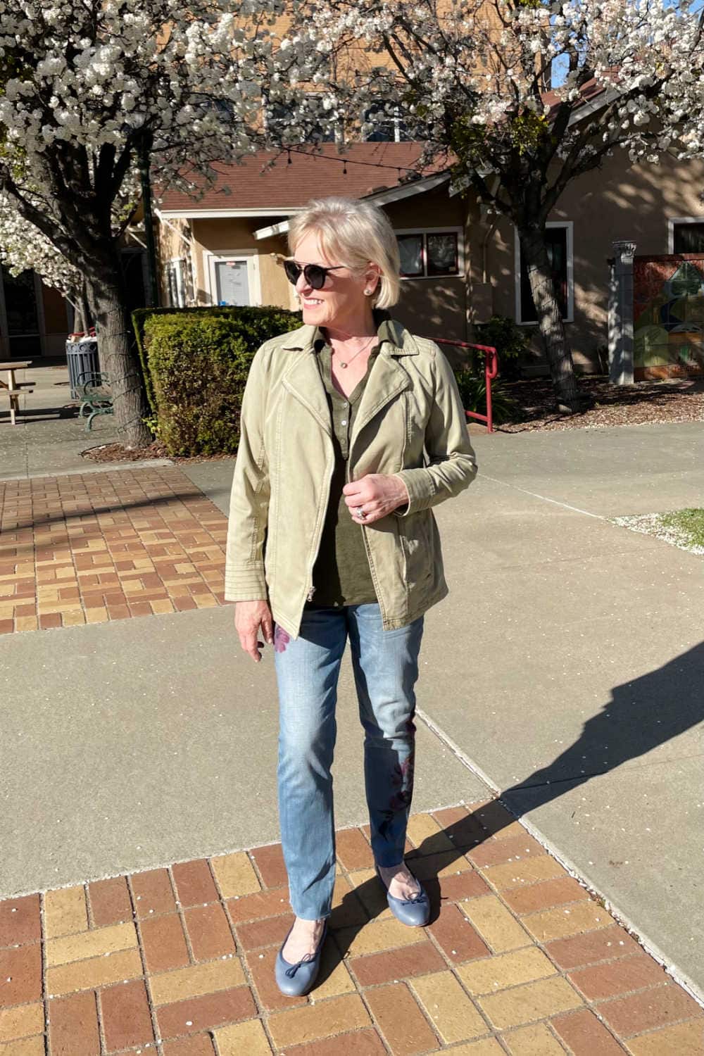 woman walking on brick walkways wearihng green jacket and blue jeans