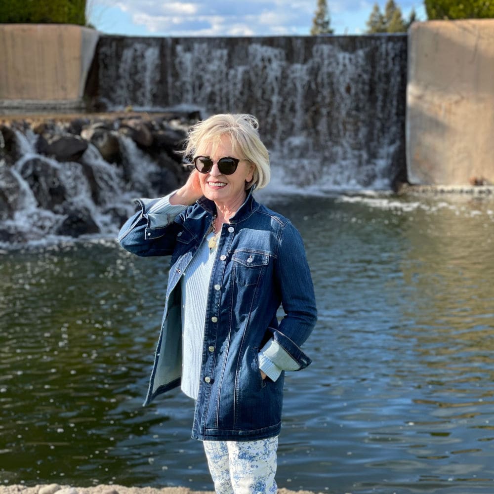 woman standing in front of waterfall wearing denim jacket