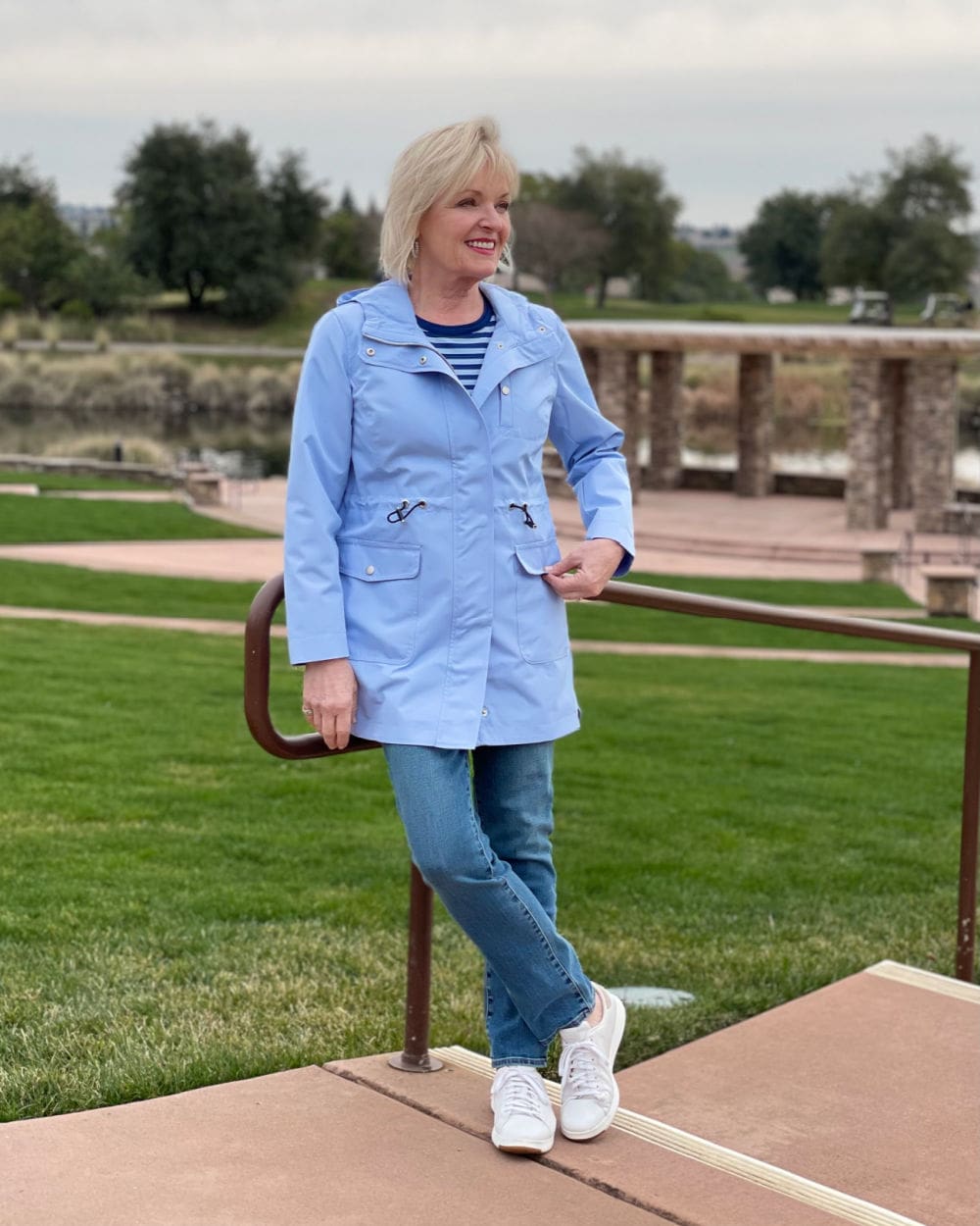 woman leaning on railing wearing striped tee, blue jeans and coated canvas anorak