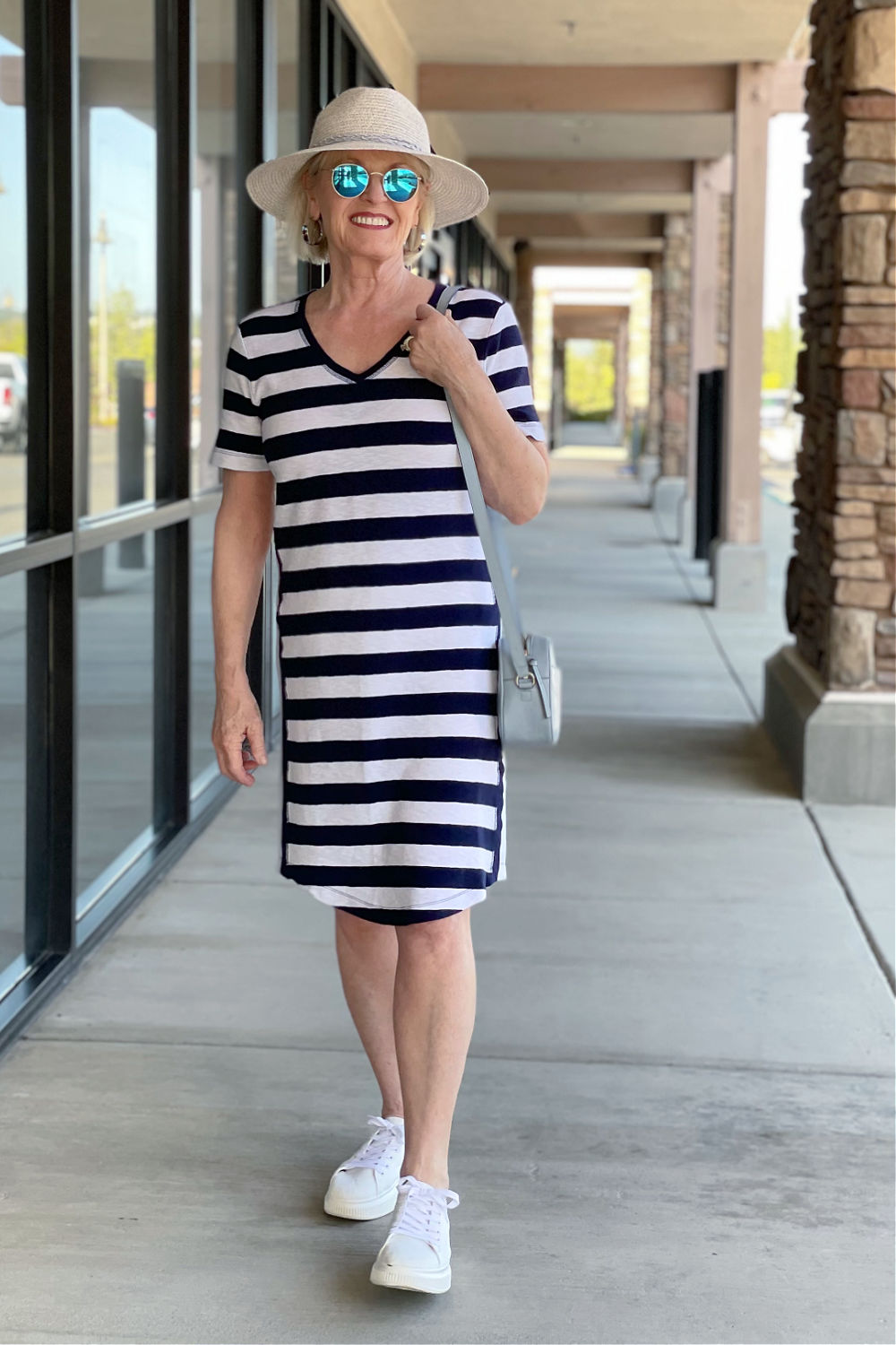 woman walking wearing navy and white striped dress with blue hat and white sneakers