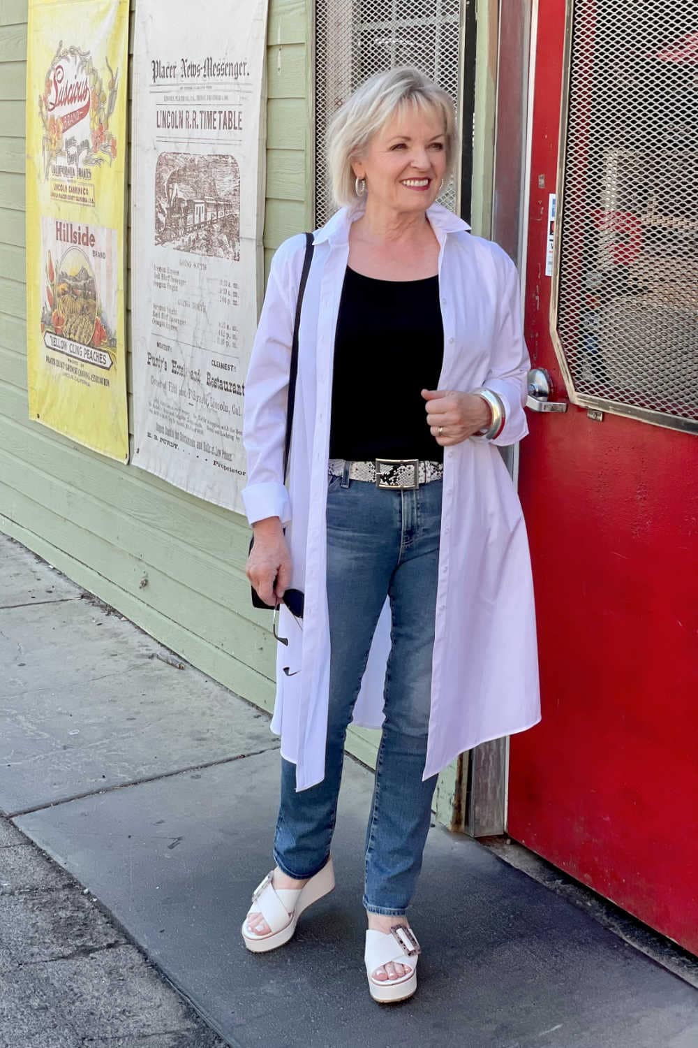 WOMAN STANDING IN FRONT OF RED DOOR WEARING WHITE DUSTER AND BLUE JEANS