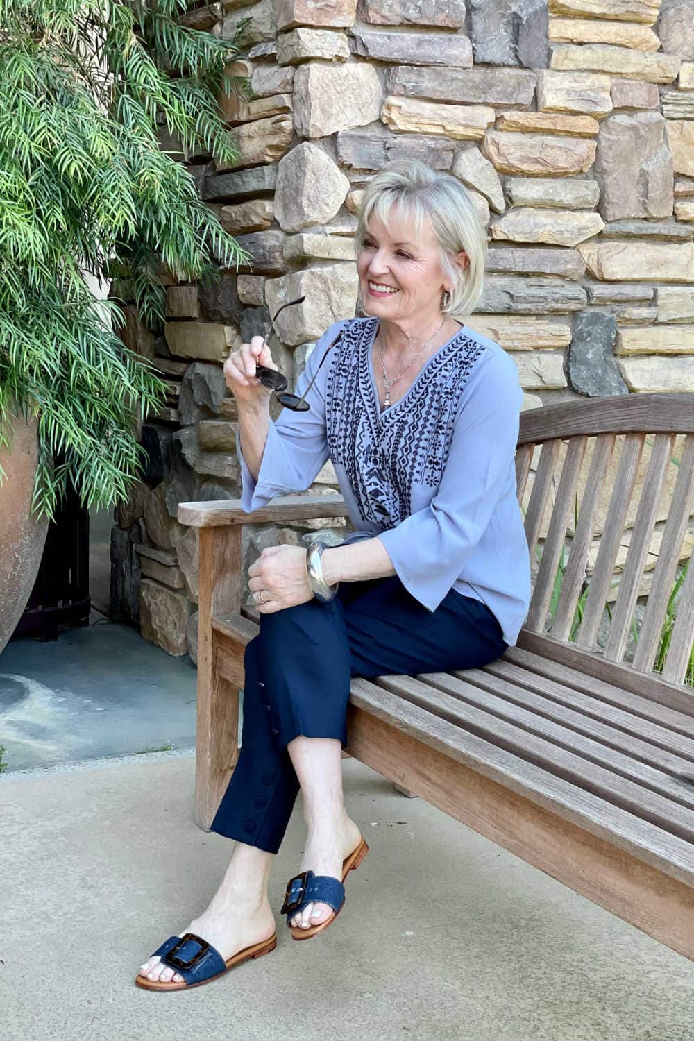 woman sitting on bench wearing denim slides and purple top