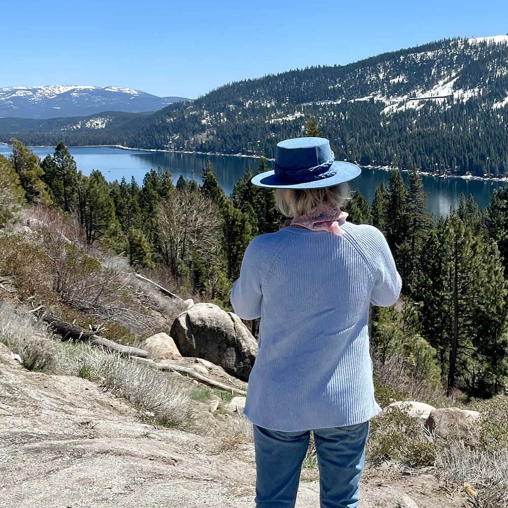 woman wearing denim hat and blue jeans looking over Donner Lake.