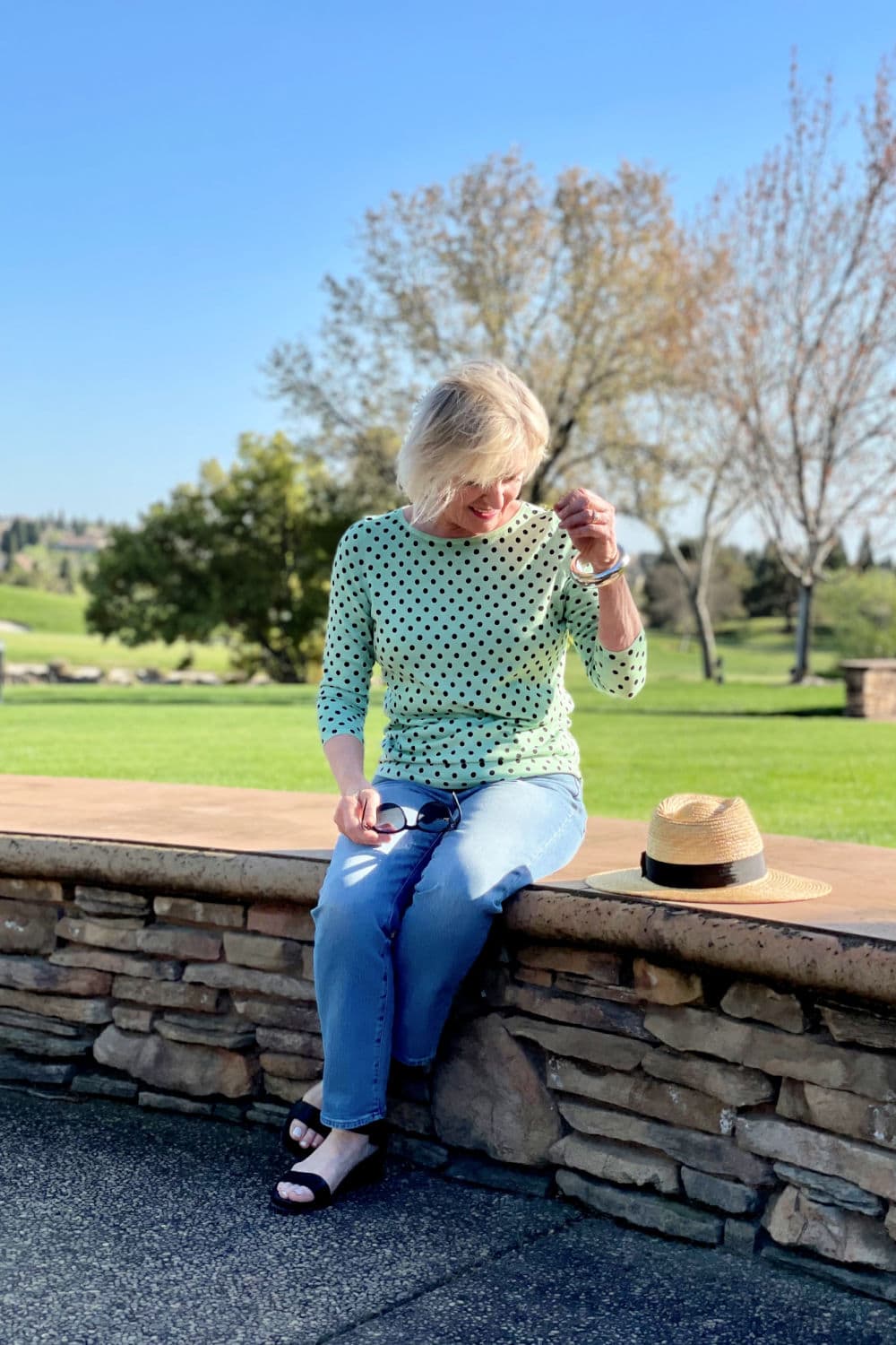 woman sitting on bench wearing green dot sweater and pale blue jeans