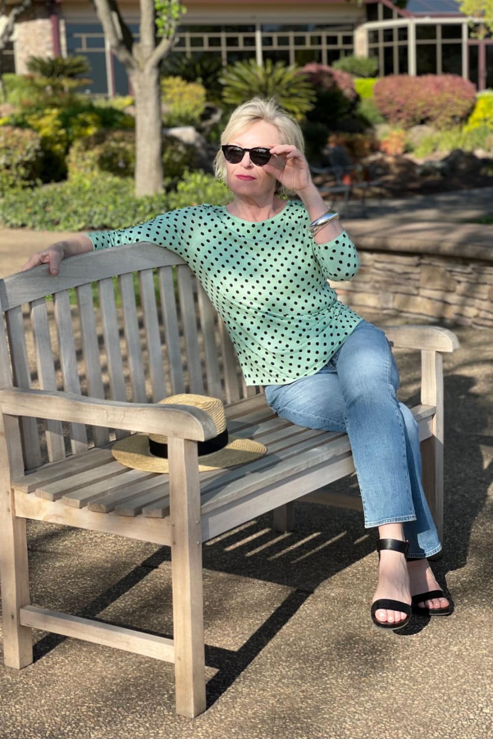 blonde woman sitting on park bench wearing green dot sweater and jeans