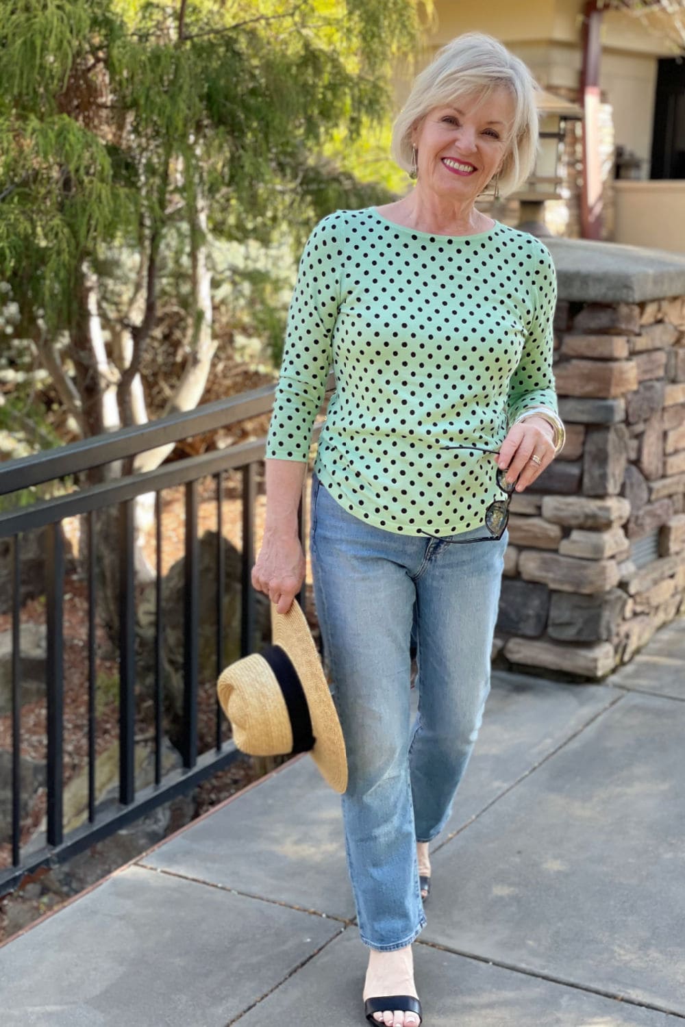 woman walking near fountain wearing green sweater and blue jeans