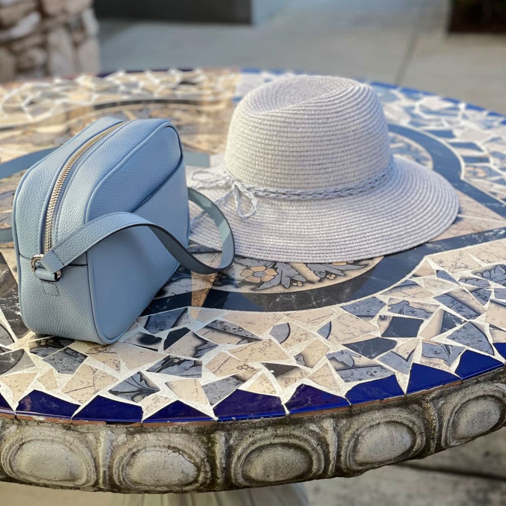blue cross body bag and blue straw hat on table
