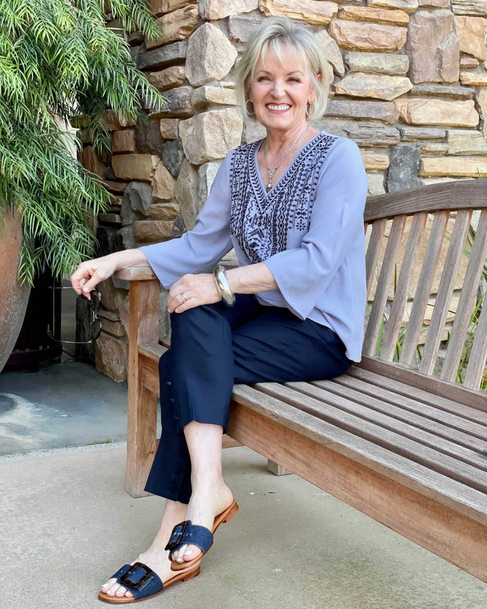 woman sitting on park bench wearing linen pants boho top and denim shoes