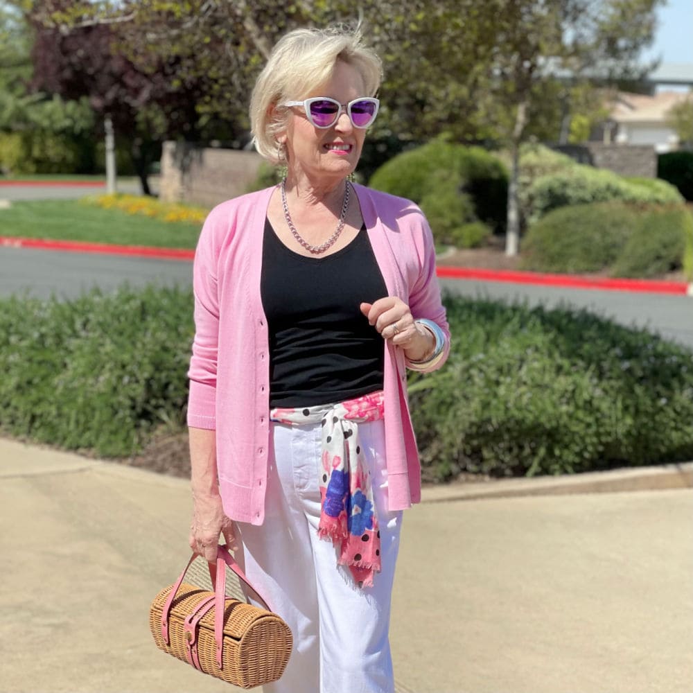 woman standing in sun carrying wicker handbag and wearing pink sweater