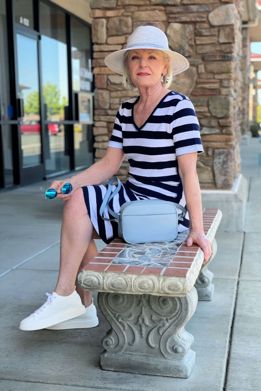 blonde woman sitting on bench wearing striped dress and straw hat