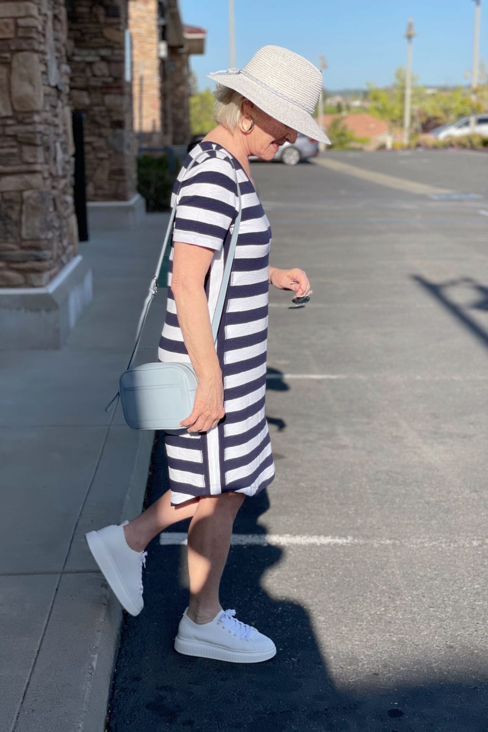 woman stepping off curb wearing tee shirt dress and straw hat