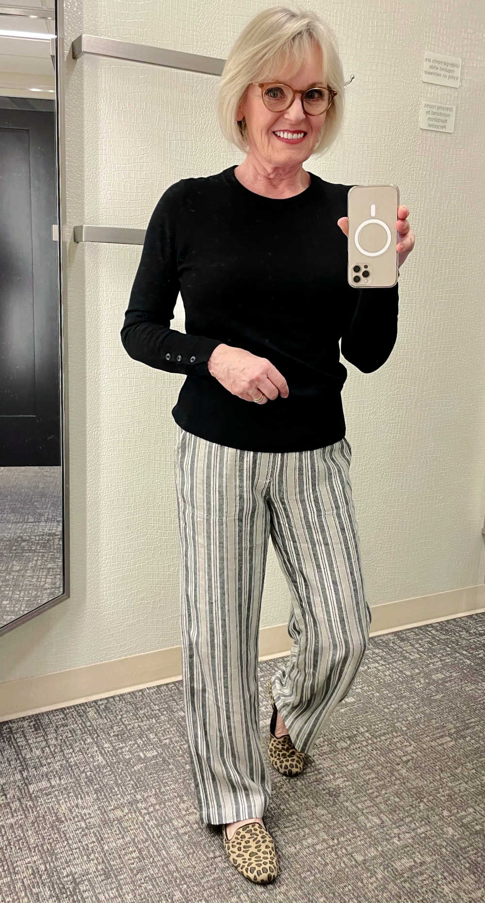 woman taking selfie in mirror wearing black sweater and striped linen pants