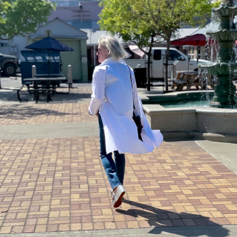 woman walking away wearing white duster and blue jeans