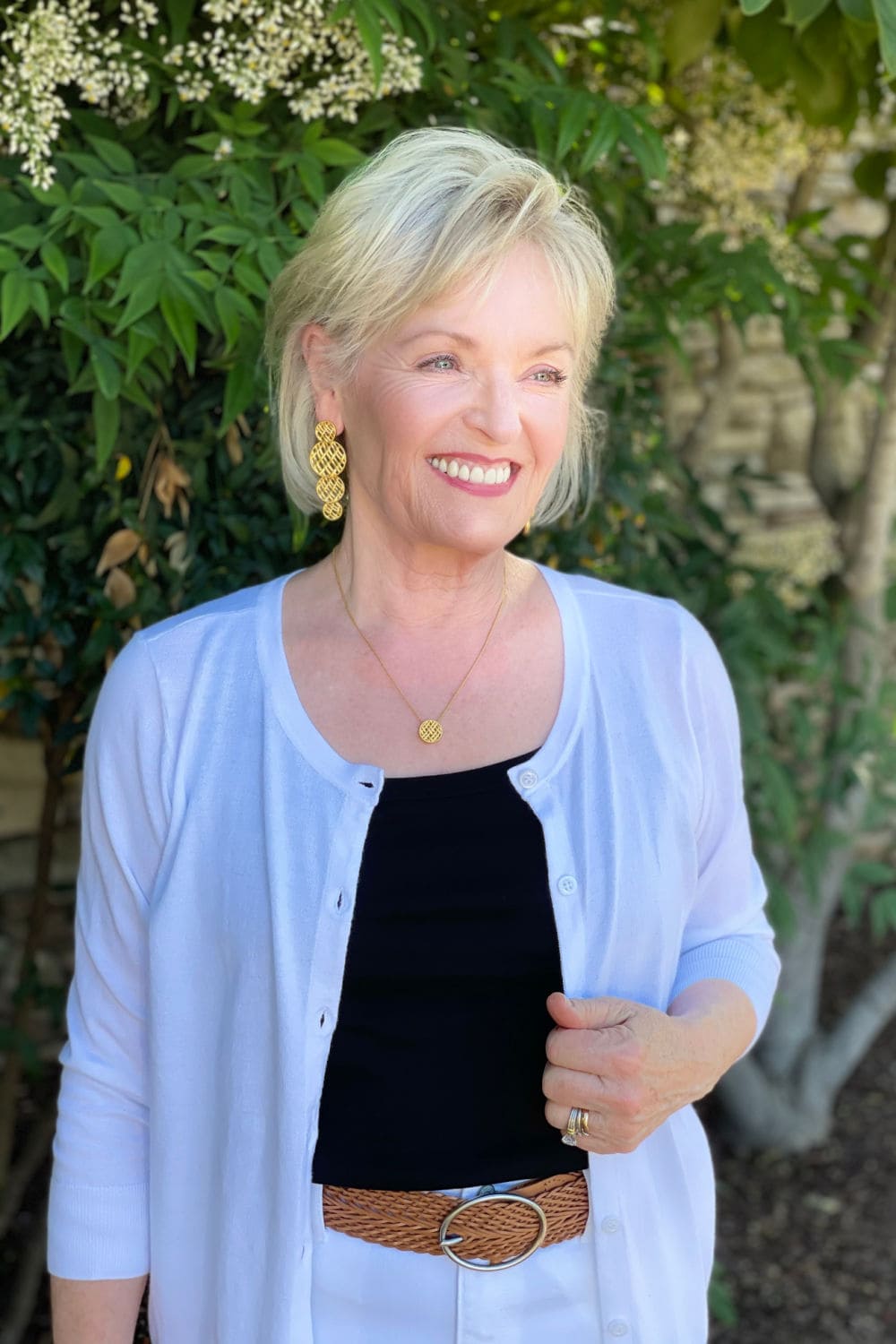 blonde woman wearing white cardigan, black tank and gold earrings