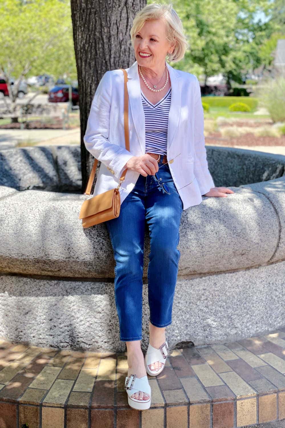 woman sitting on cement wall wearing jeans, blazer and striped tee