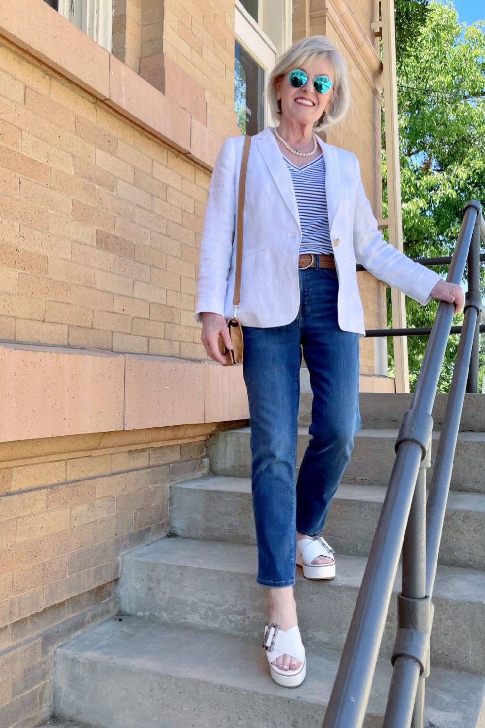 blonde woman walking downstairs weaing linen blazer and blue jeans with white sandals