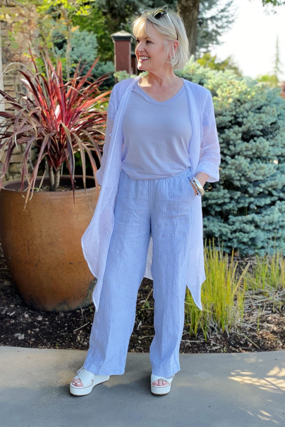 jennifer of a well styled life wearing purple tee, linen cardigan and line pants in front of gate