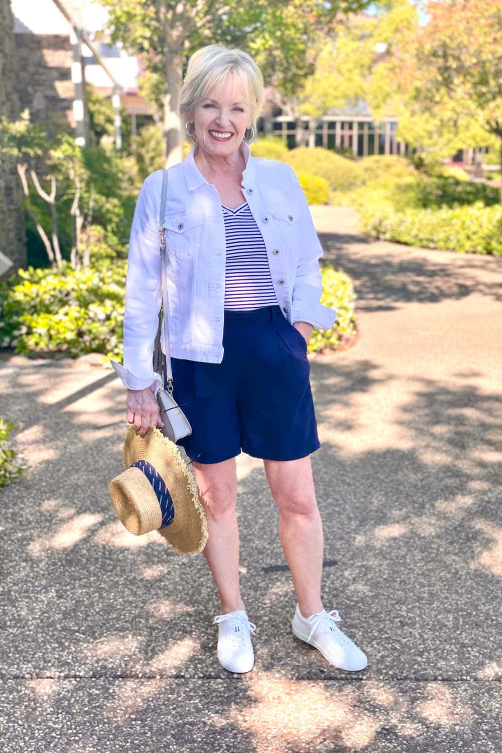 woman wearign whte denim jacket, navy pleated shorts and white sneakers