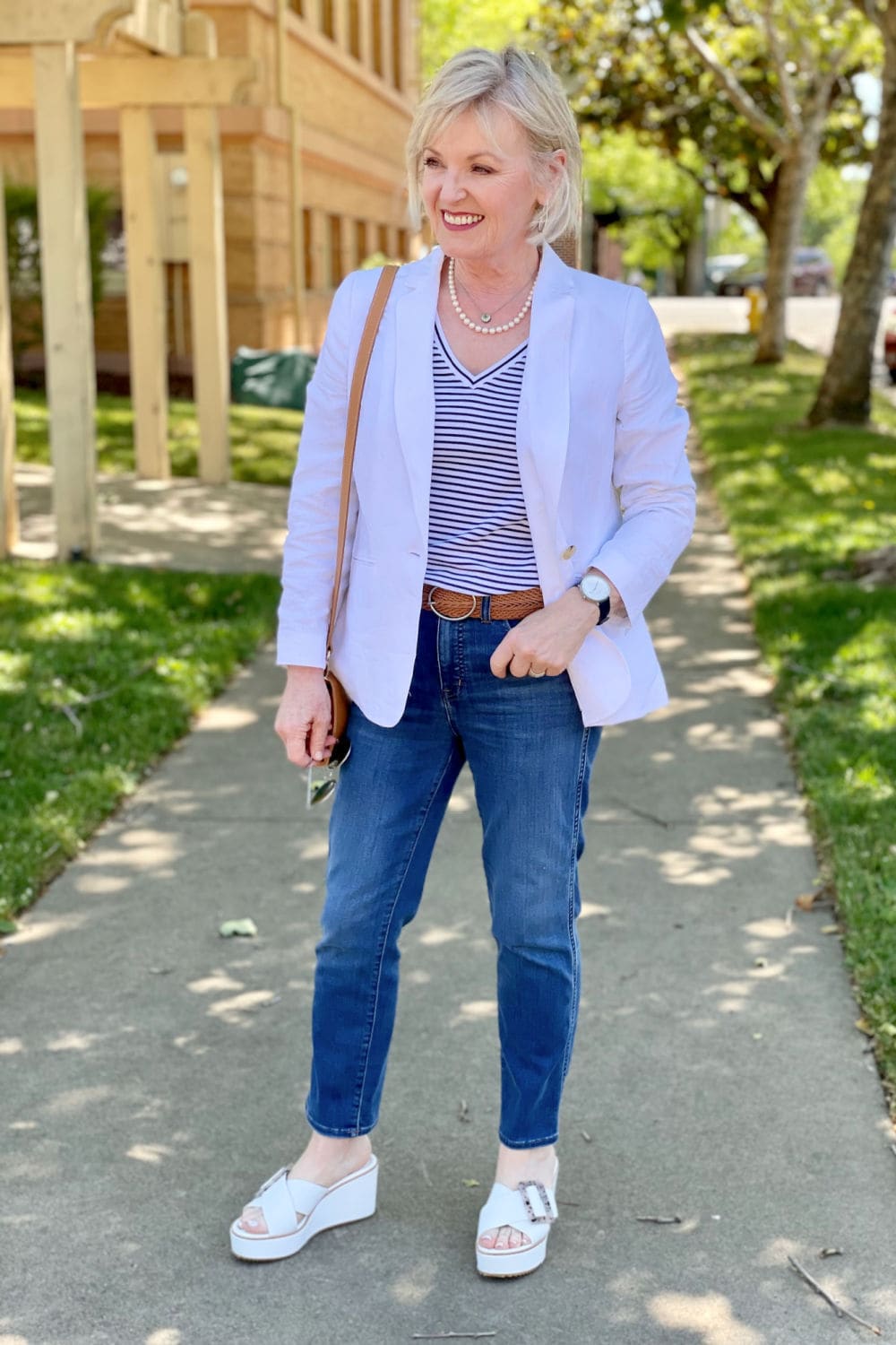 woman on sidewalk smiling at camera wearing mirrored sunglasses, jeans and striped tee