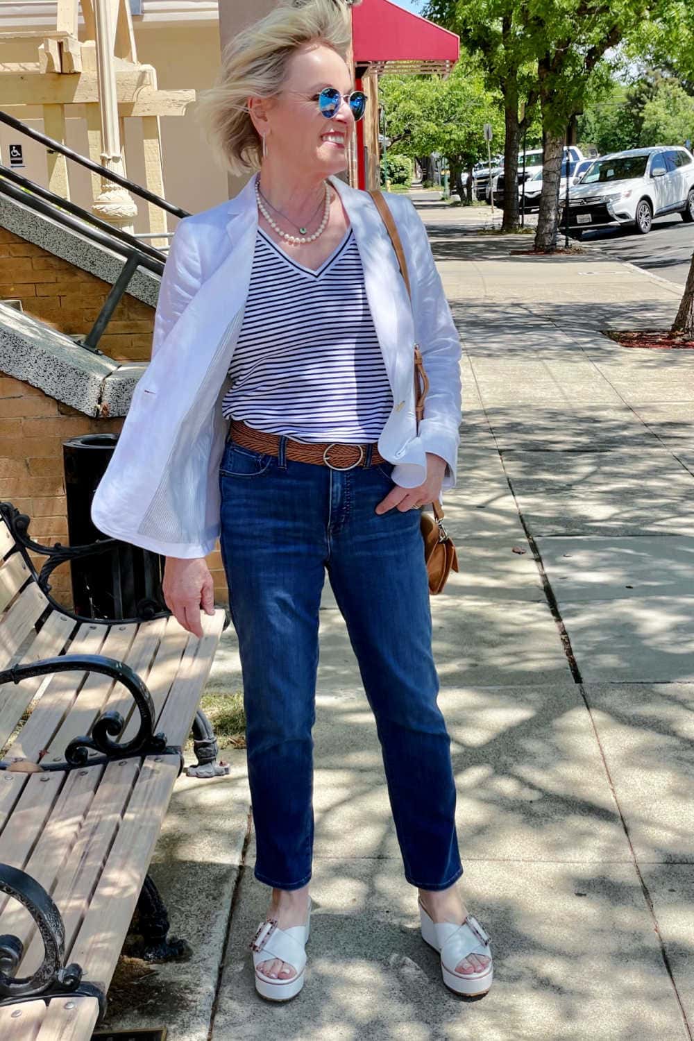woman walking down street in striped tee, blue jeans and white jacket