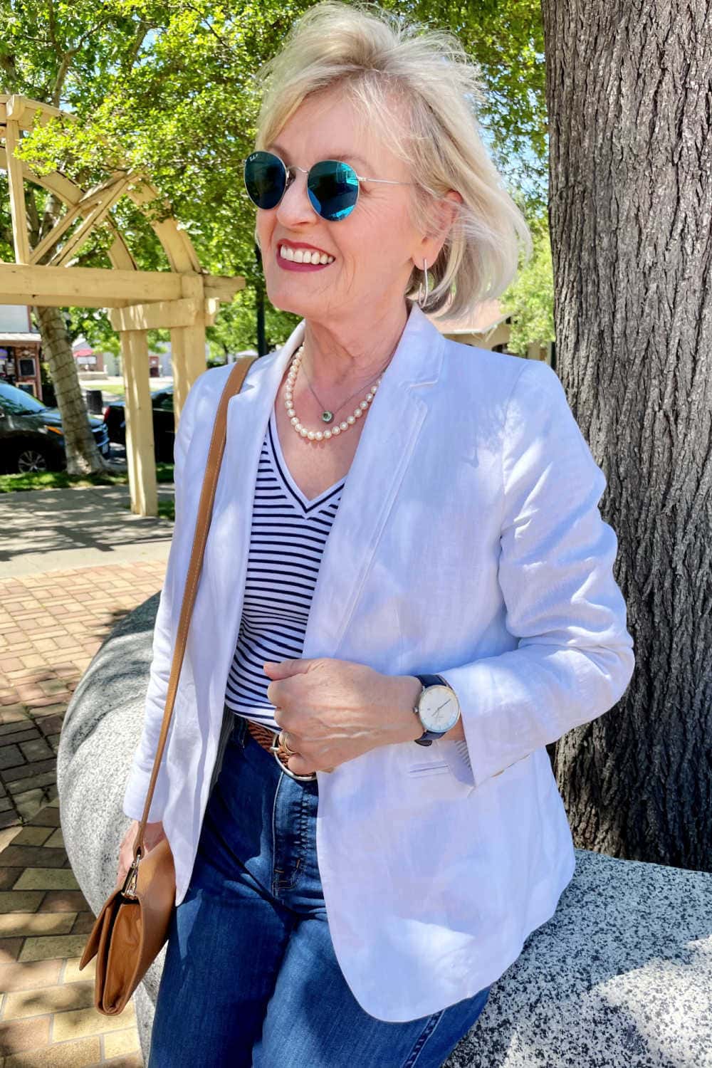 woman wearing striped tee, white blazer and pearls sitting by tree