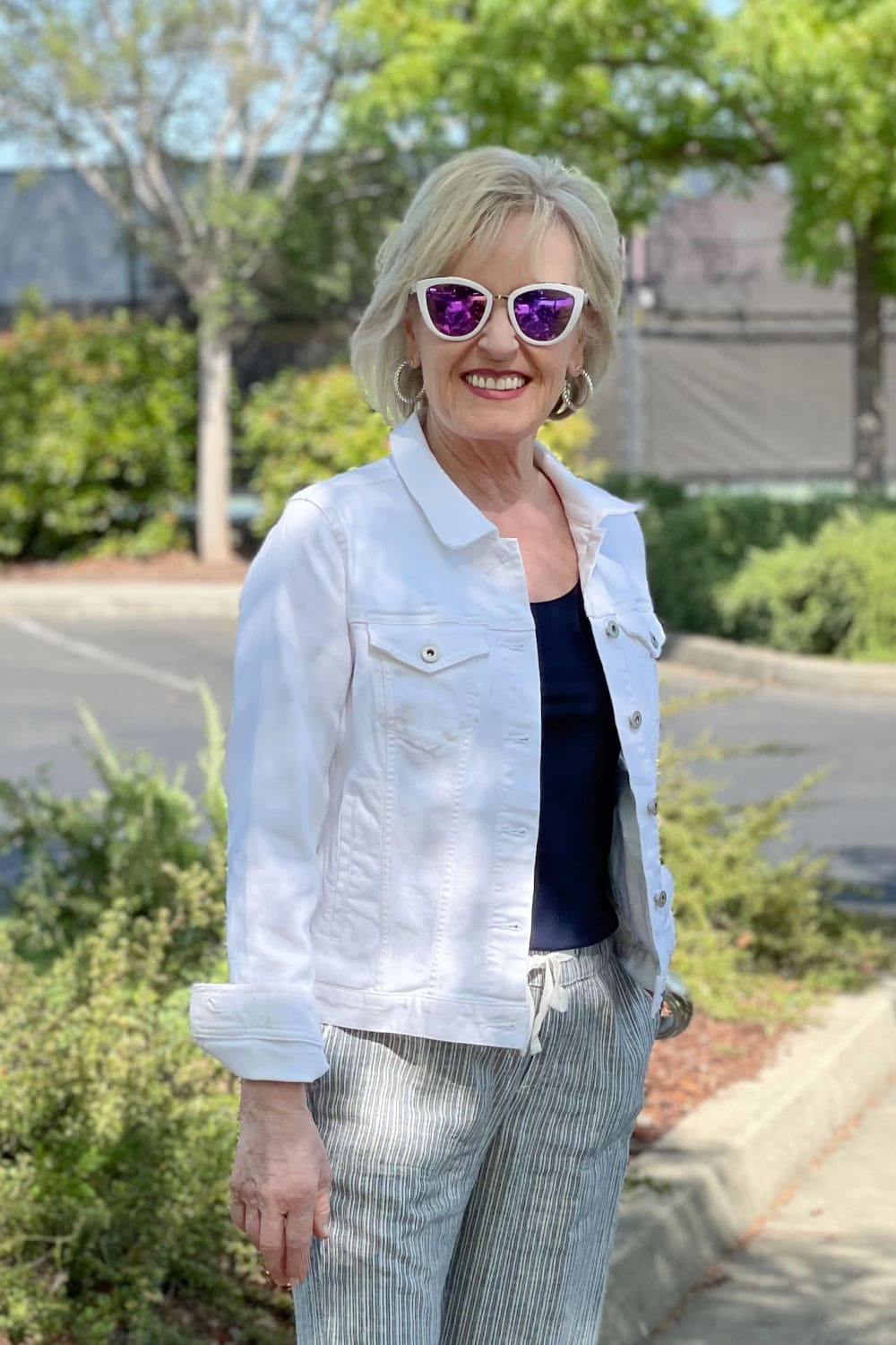 woman wearing white mirrored sunglasses, navy top and white denim jacket