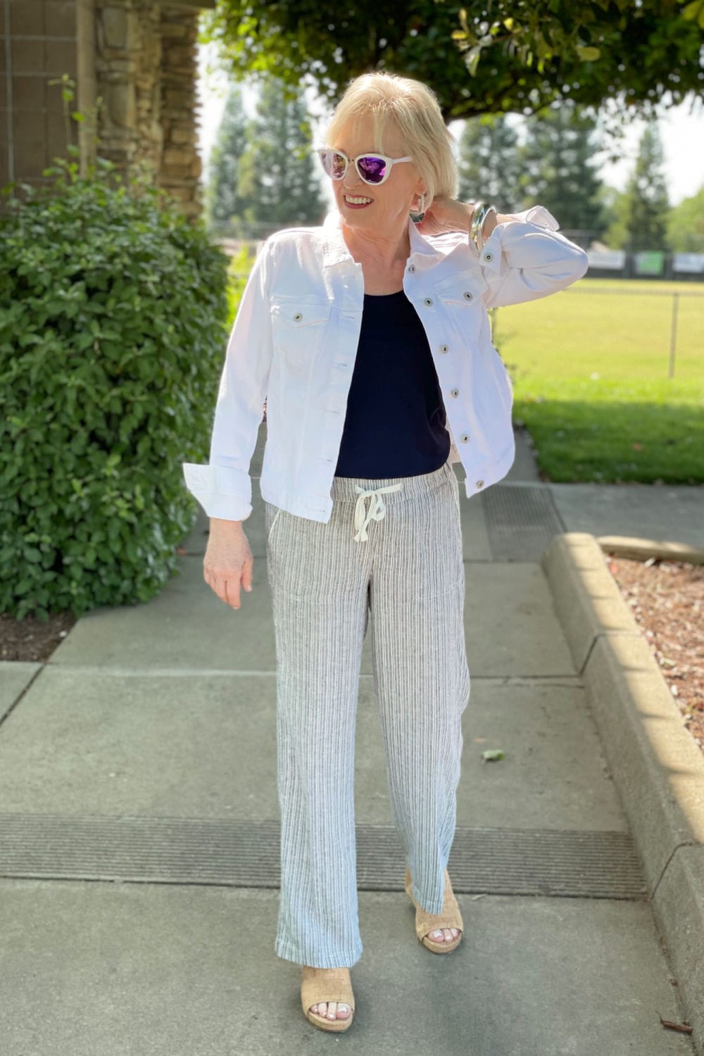 woman walking on path adjusting collar of white denim jacket