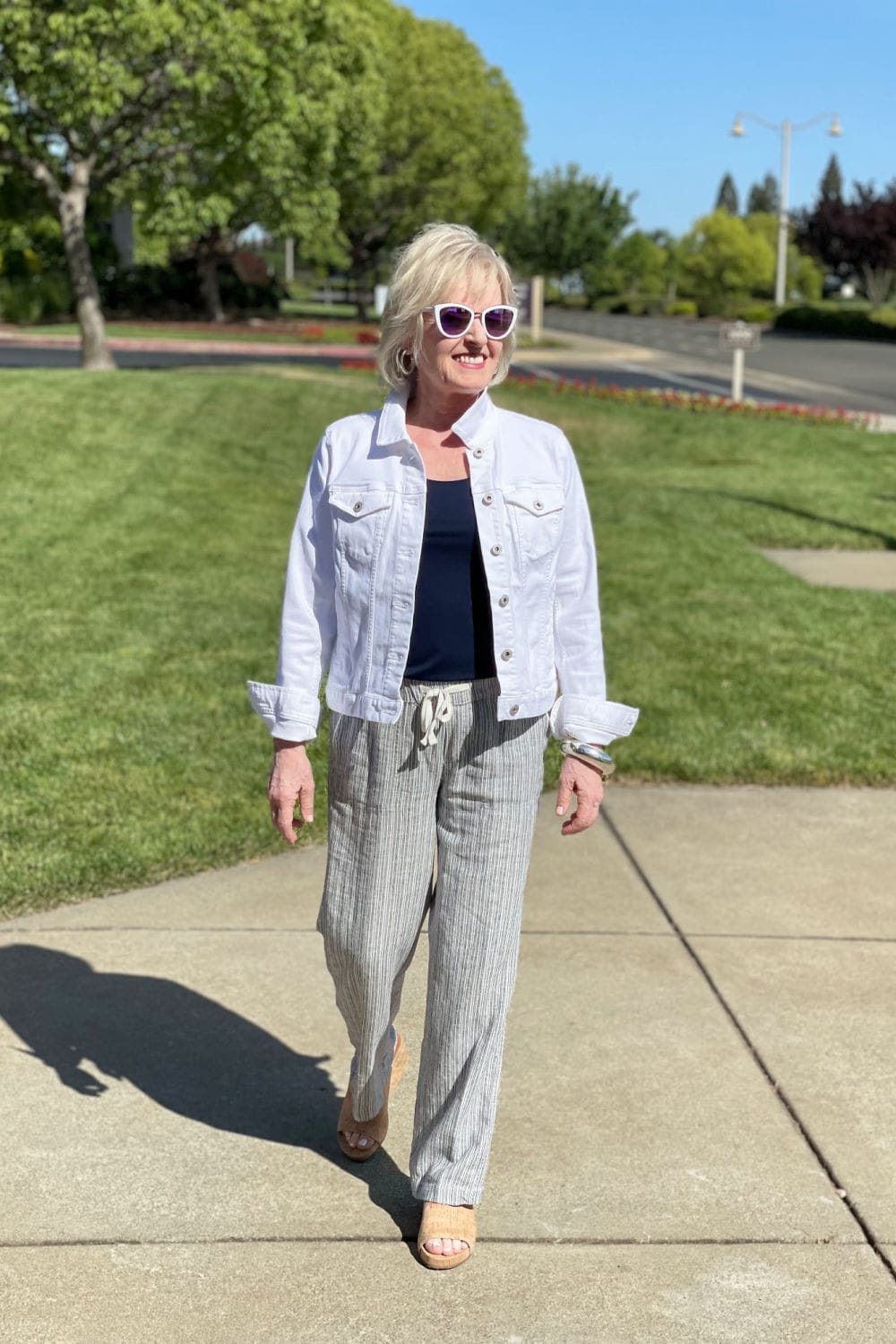 blonde wonman walking down sidewalk wearing white denim jacket and navy linen pants