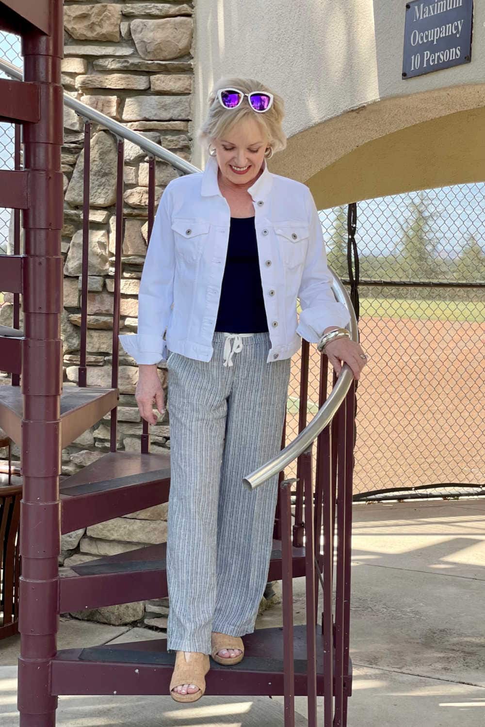 blonde woman walking down spiral staircase wearing white jacket, striped pants and cork wedges