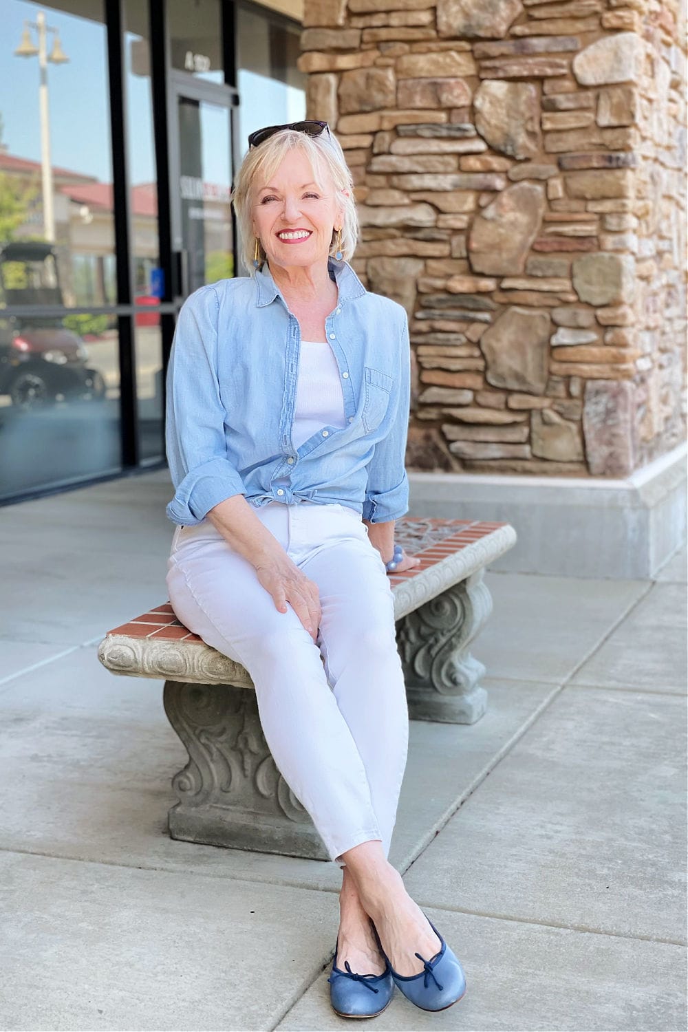 blonde woman sitting on bench wearing classic white denim jeans with chambray shirt