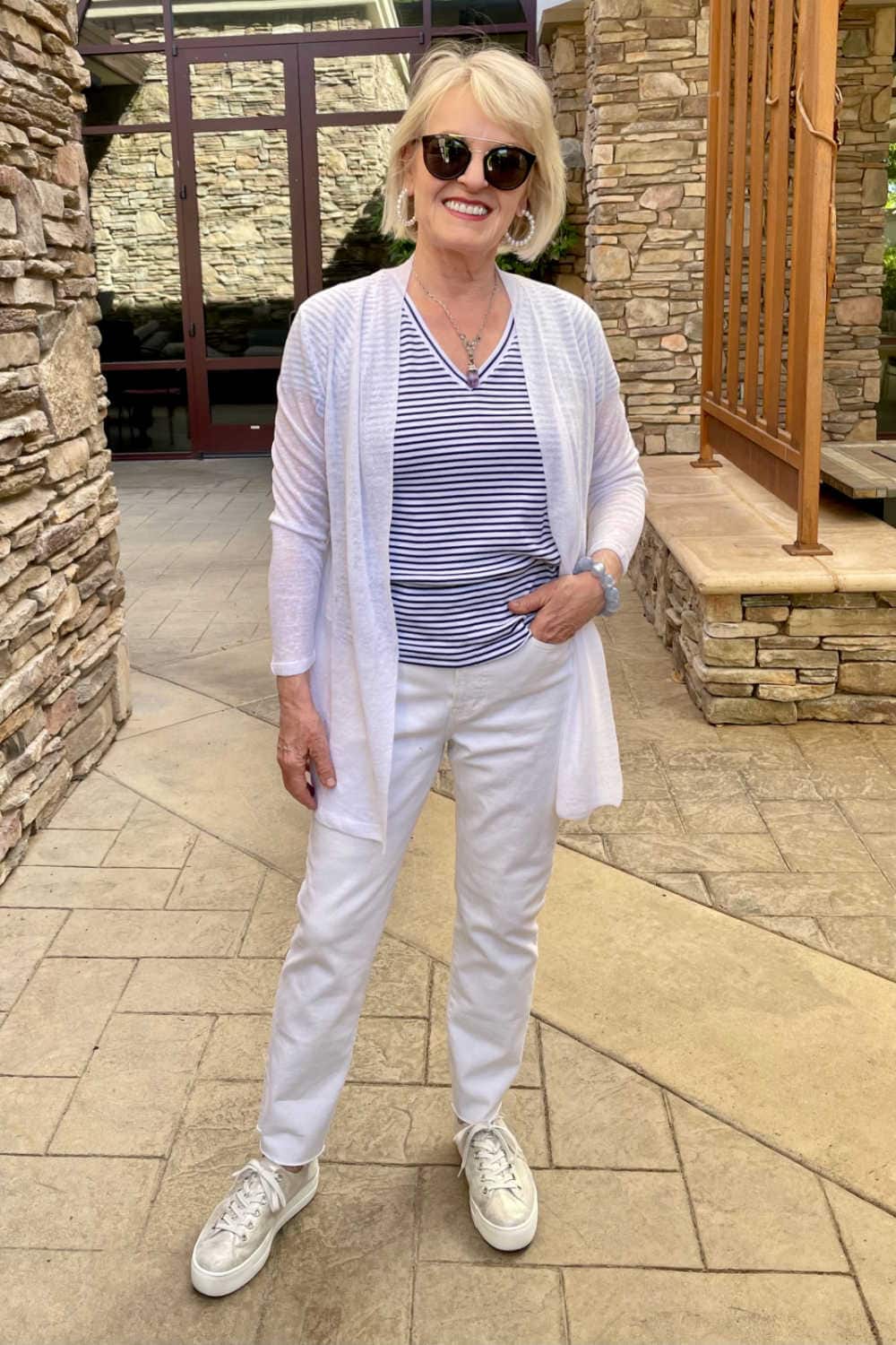blonde woman wearing white sweater, white jeans and gold sneakers in patio
