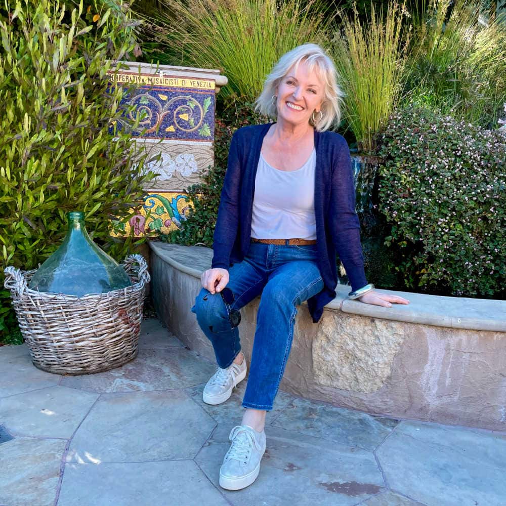 over fifty blogger jennifer connolly sitting on wall wearing blue cardrigan and blue jeans