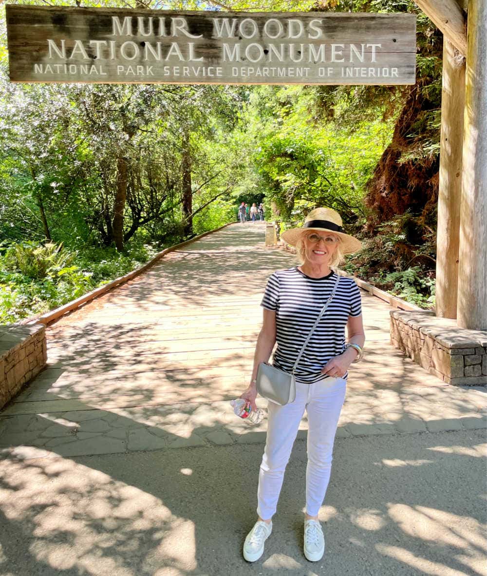 woman standing under muir woods sign wearign straw hat