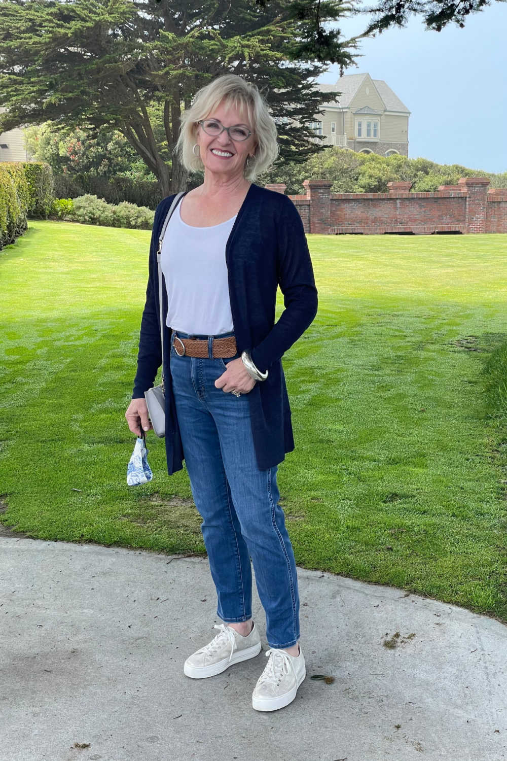 woman standing in jeans and blue sweater in front of lawn and hotel at half moon bay