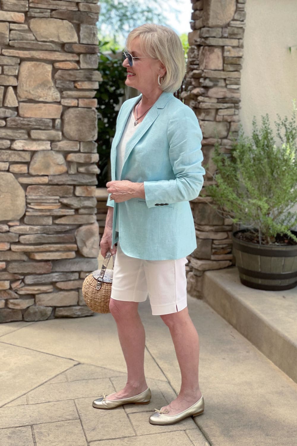 sideways view of blonde woman wearing aqua blazer and white shorts with gold shoes