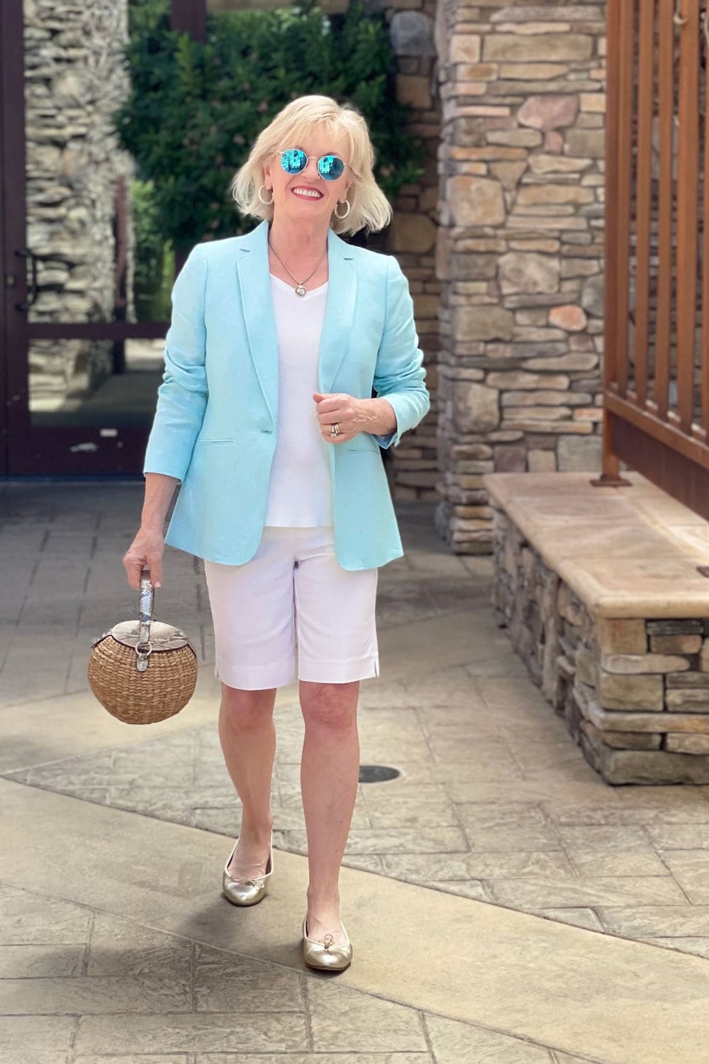 over 50 blogger walking toward the camera in linen blazer, gold flats and white shorts