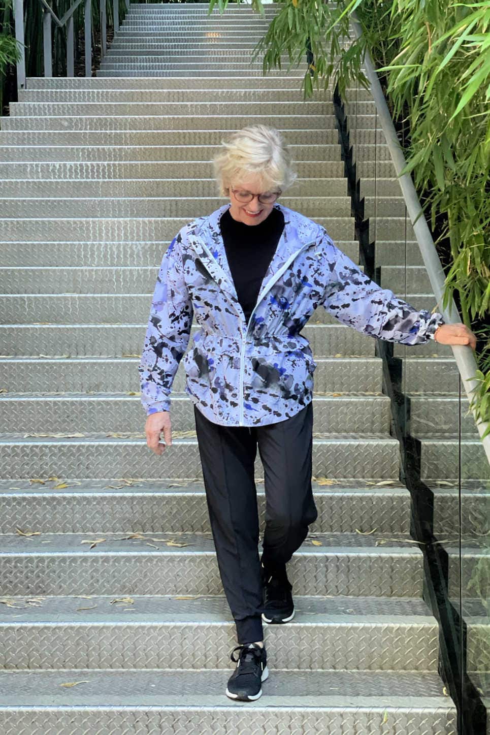 blonde woman walking down stairs wearing nylon jacket, top and pants