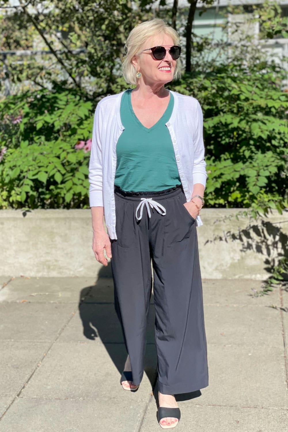 woman walking toward camera wearing black pants and green tank with white cardigan