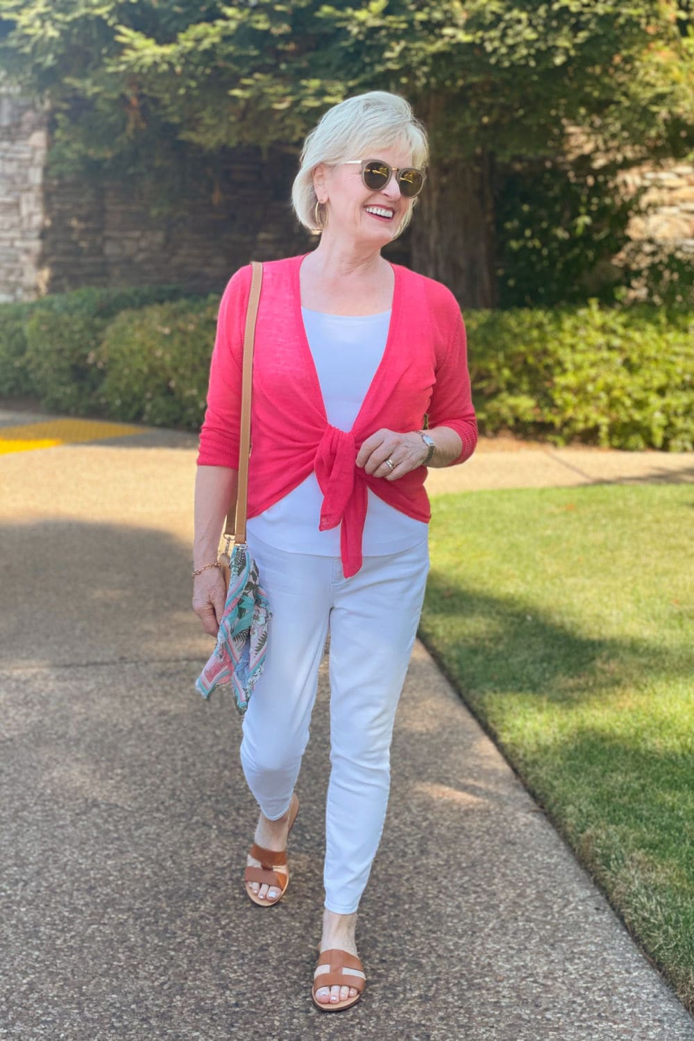 woman walking toward camera wearing white jeans and pink cardigan