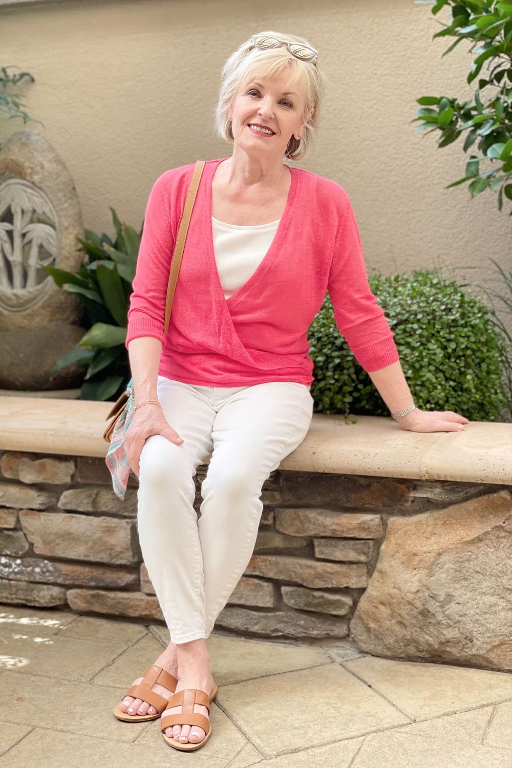 blonde woman sitting on wall wearing white jeans and tee with red sweater