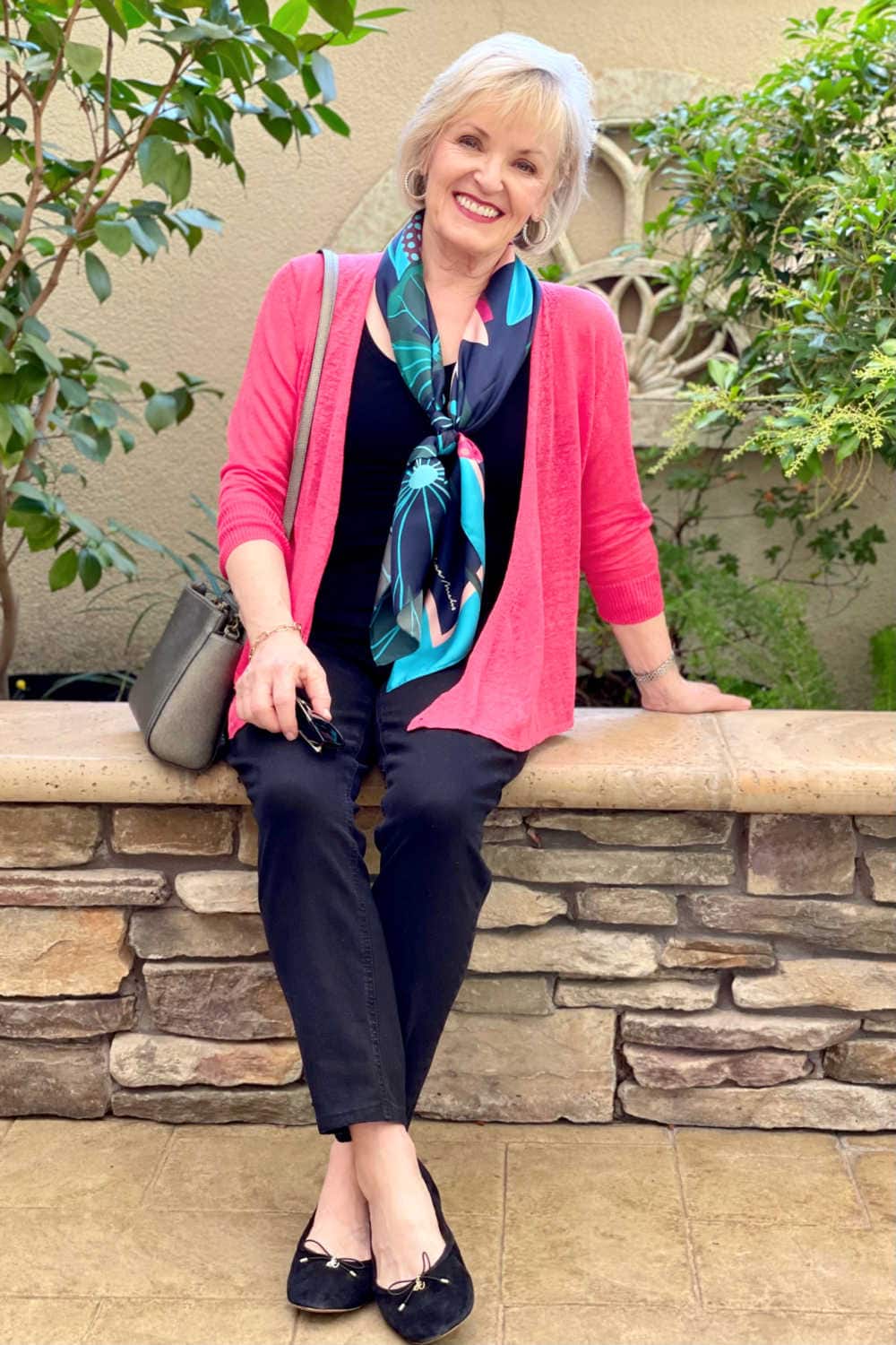 blonde woman siting on wall wearing black jeans black tee and red cardigan