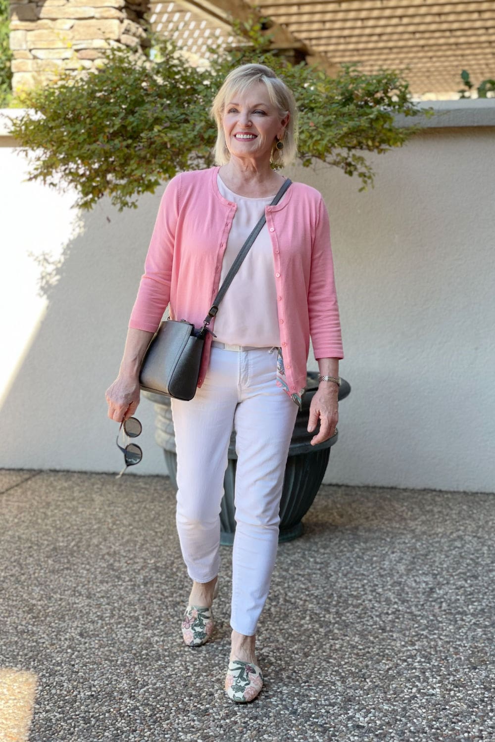 woman walking toward camera wearing salmon colored sweater and white jeans with embroidered mules
