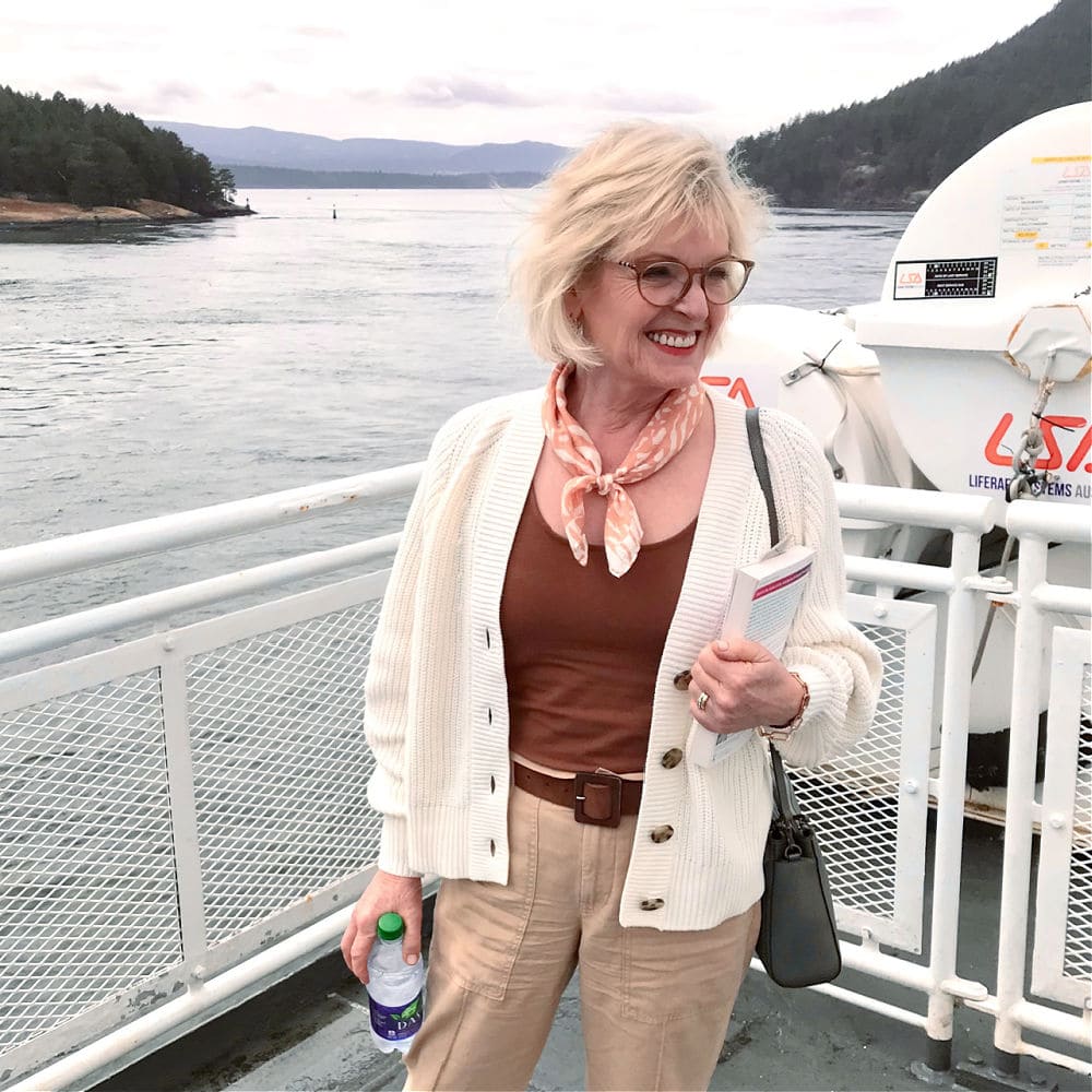 over 50 woman wearing shrunken sweater and cinnamon colored tank top on deck of ferry