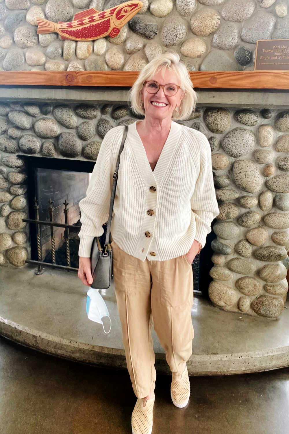 over 50 blogger wearing ivory sweater and cargo pants in front of rock fireplace