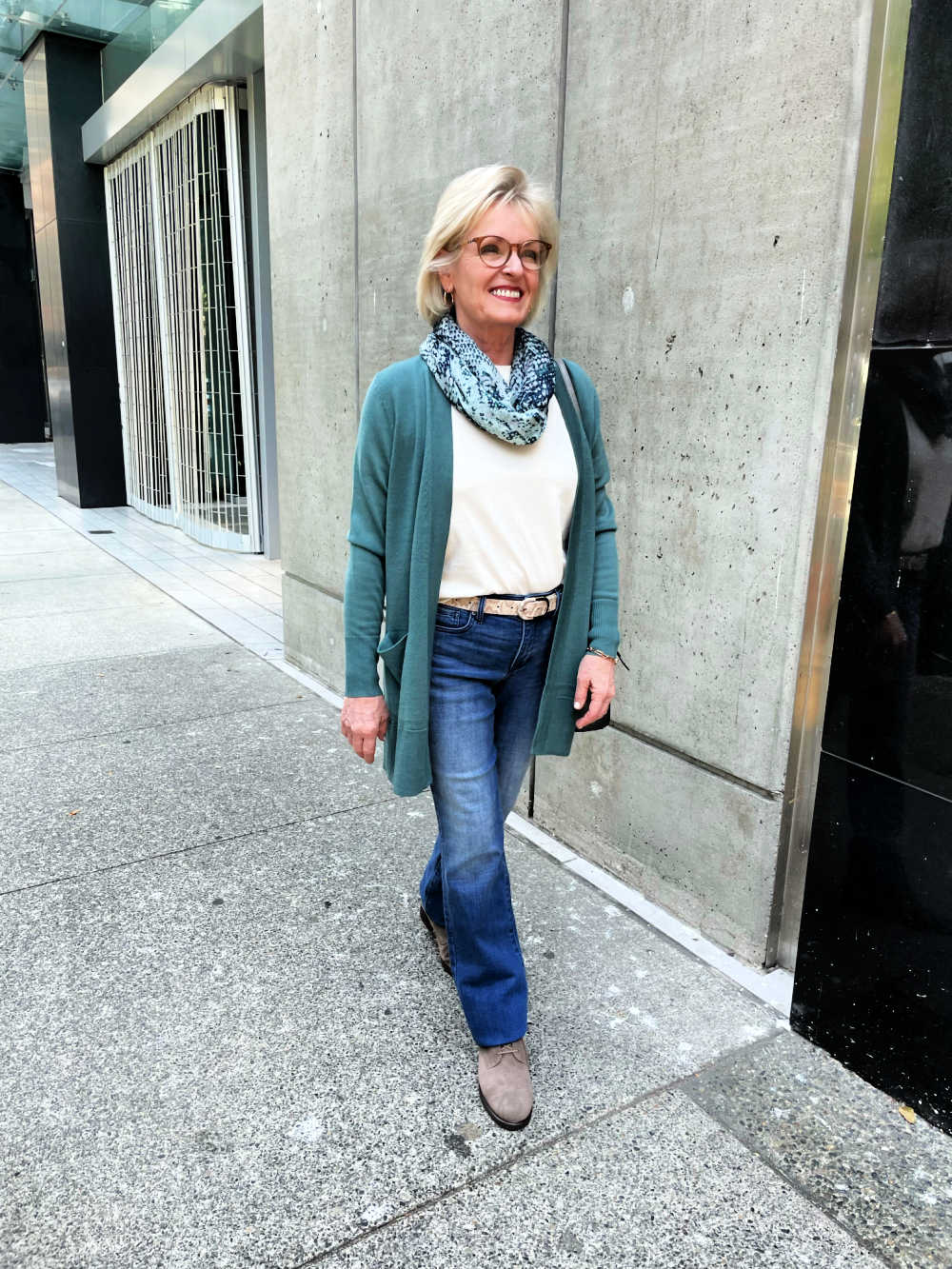 woman walking on strett wearing green cardigan, white tee, and jeans