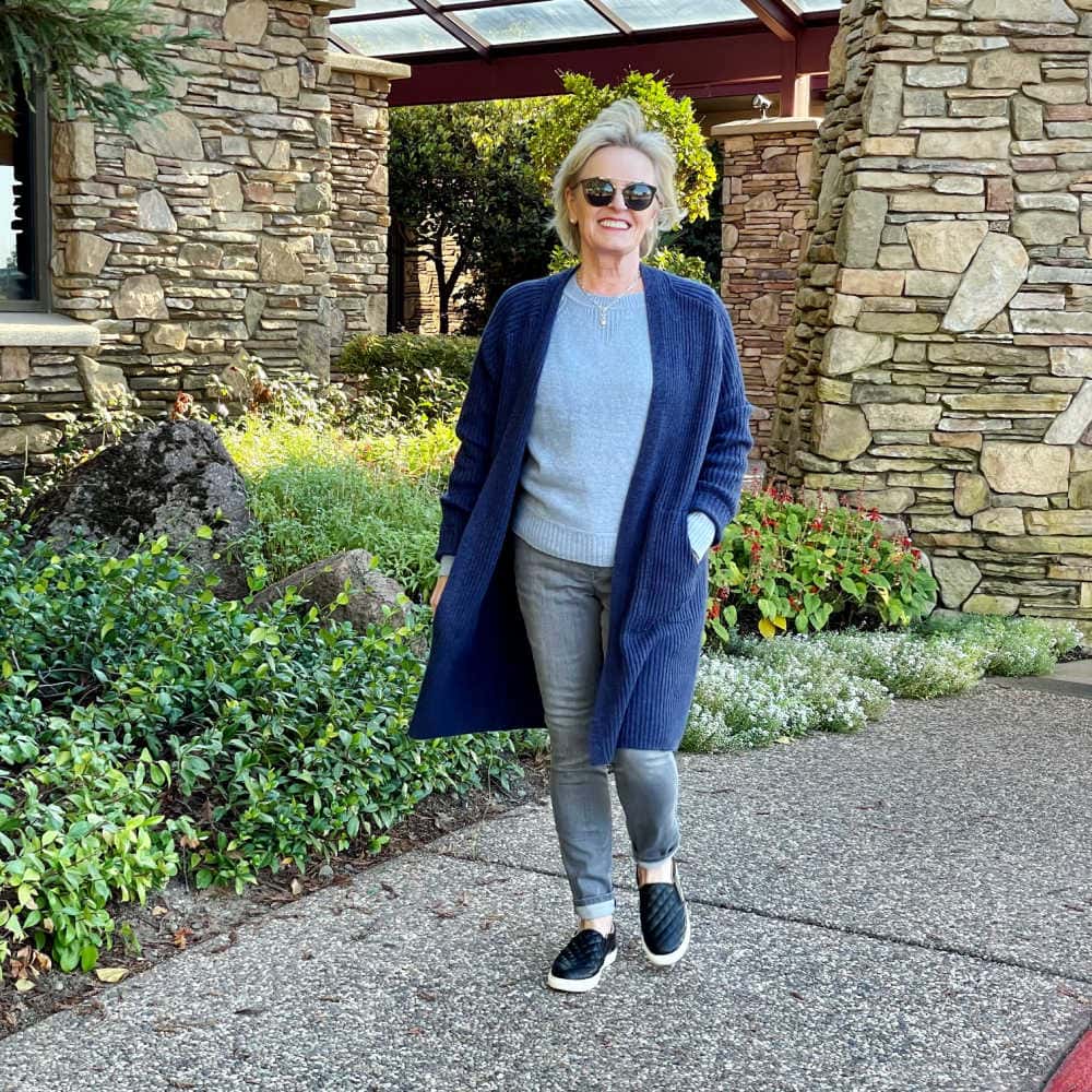 blonde woman walking wearing budget friendly long blue cardigan over blue sweater and gray jeans